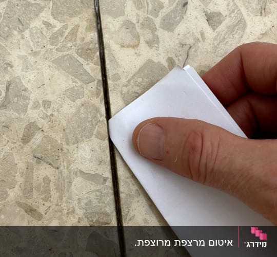 יד מחזיקה נייר על חריץ ברצפה